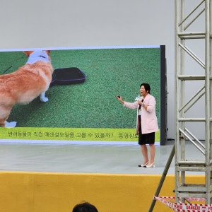 야외 무대 대형 화면 앞에서 마이크를 들고 강연하는 모습